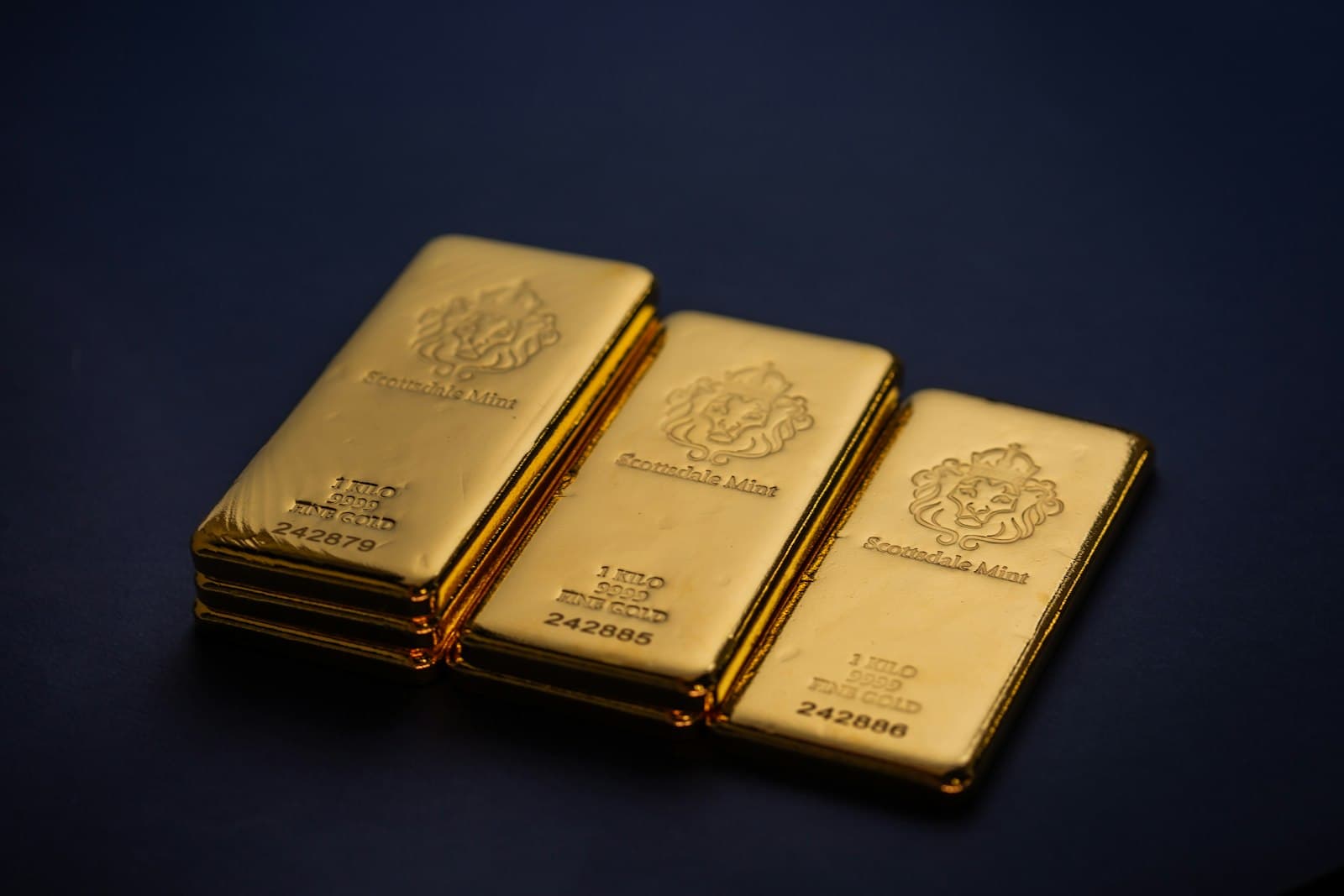 Three one-kilo gold bars on a dark navy surface